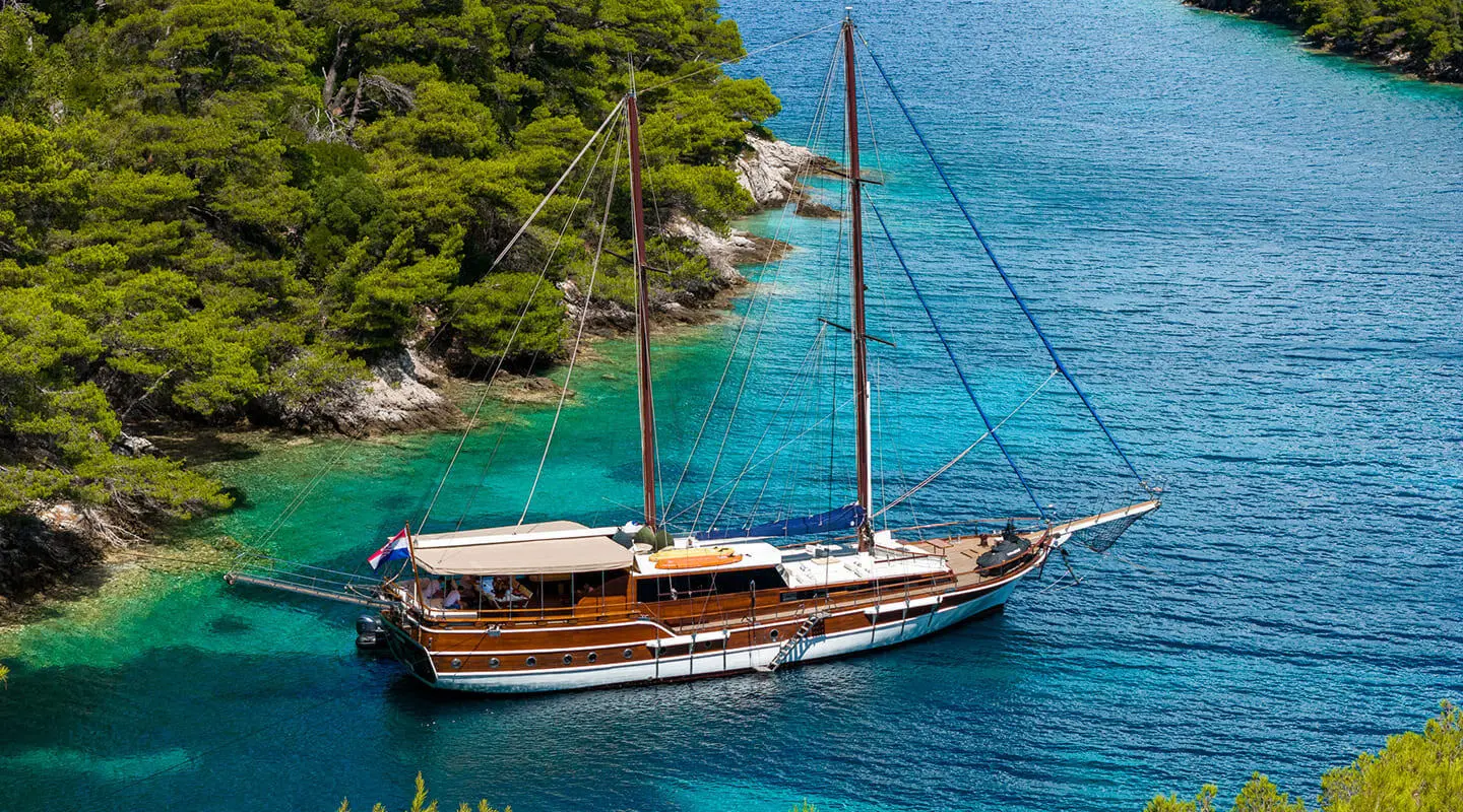 Gulet Eleganza anchored in clear blue water, wooden deck and mast visible