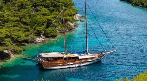 Gulet Eleganza anchored in clear blue water, wooden deck and mast visible