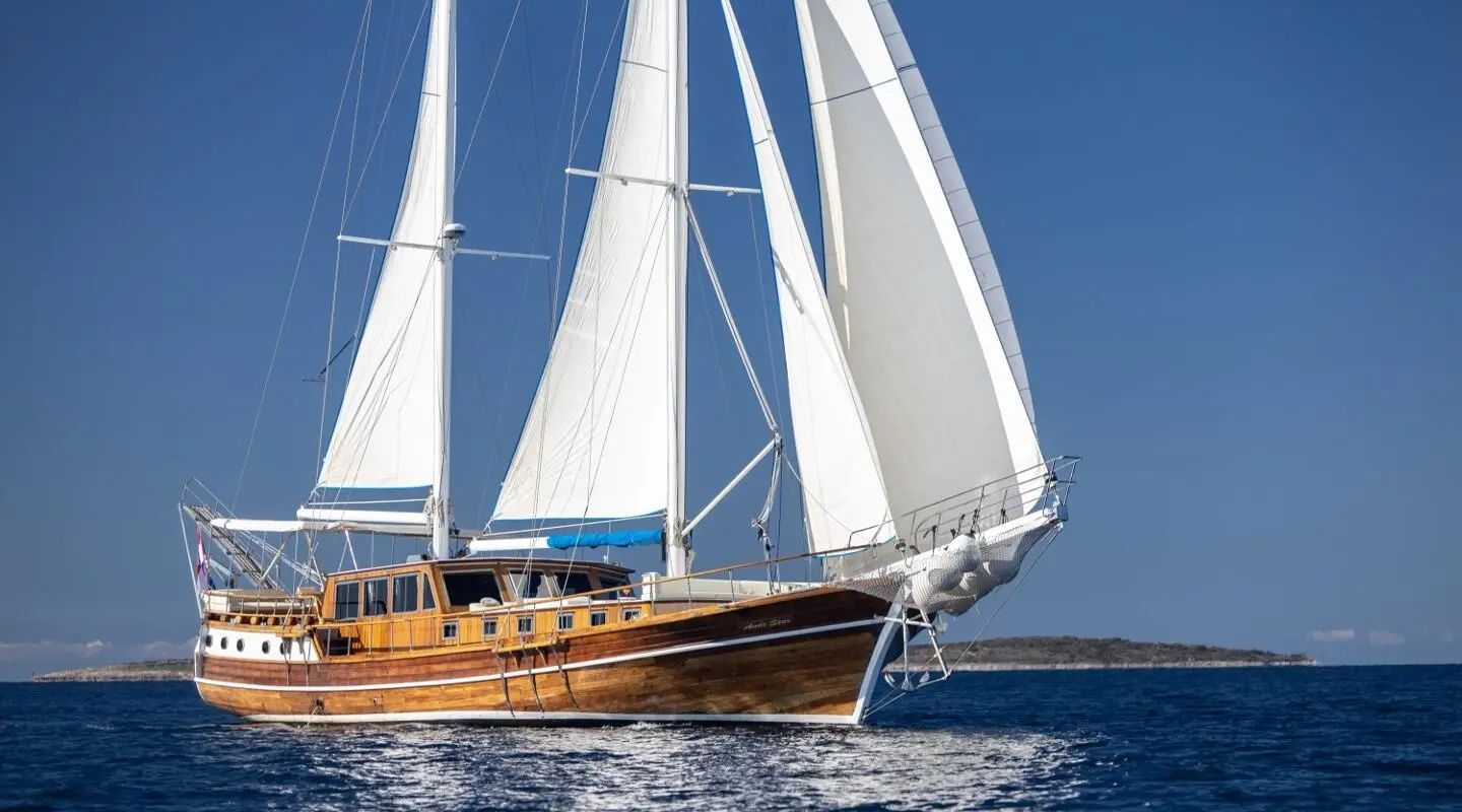 Andi Star yacht sailing with white sails and wooden deck at sea during sunset