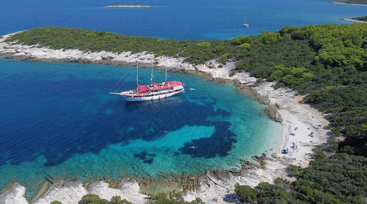 Yacht Barbara anchored on a crescent sandy bay with turquoise water
