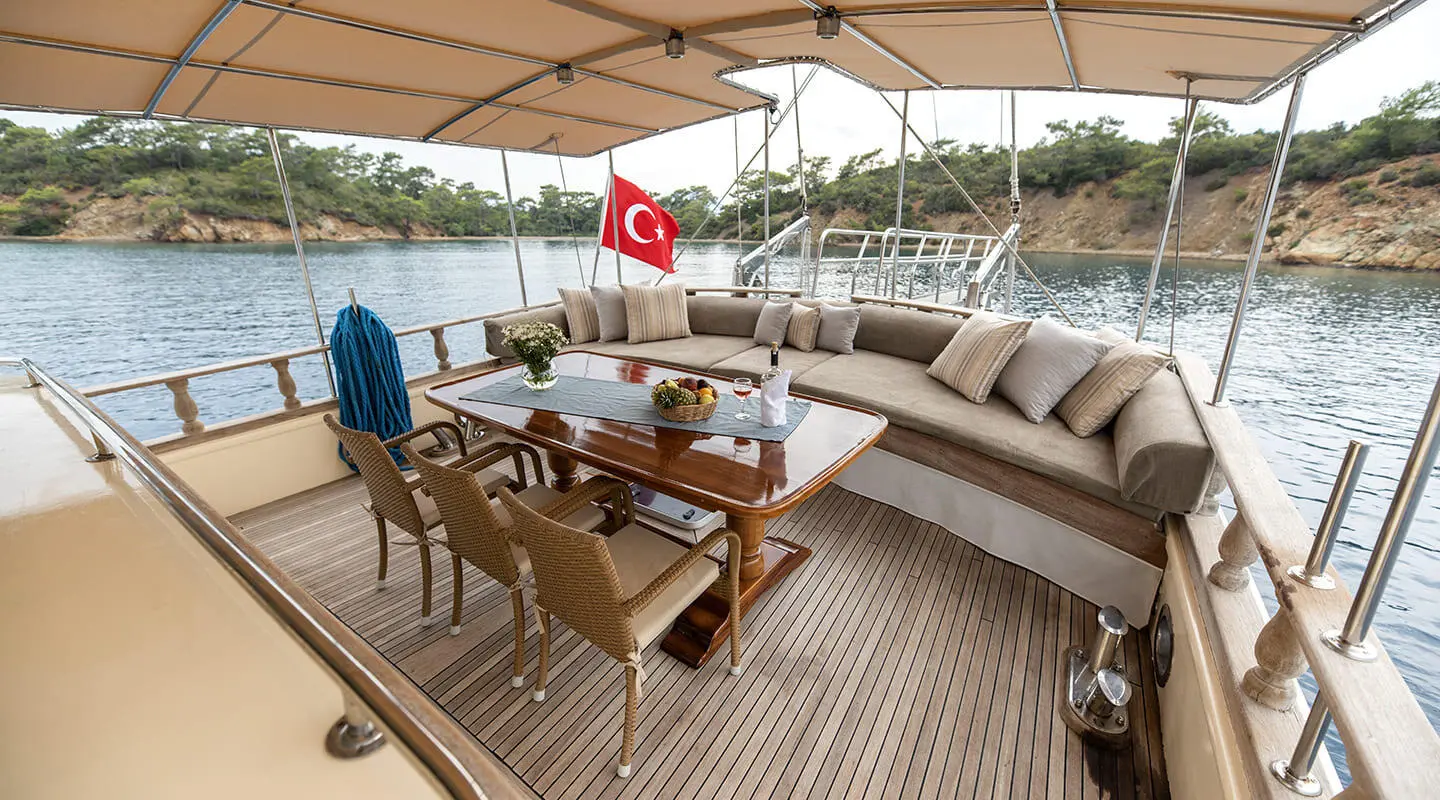 A gulet yacht Faralya aft deck with sun loungers, dining table, and umbrella under a canopy