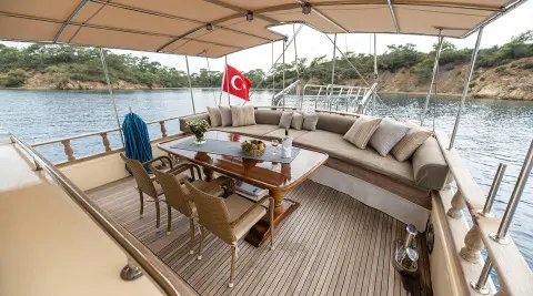 A gulet yacht Faralya aft deck with sun loungers, dining table, and umbrella under a canopy