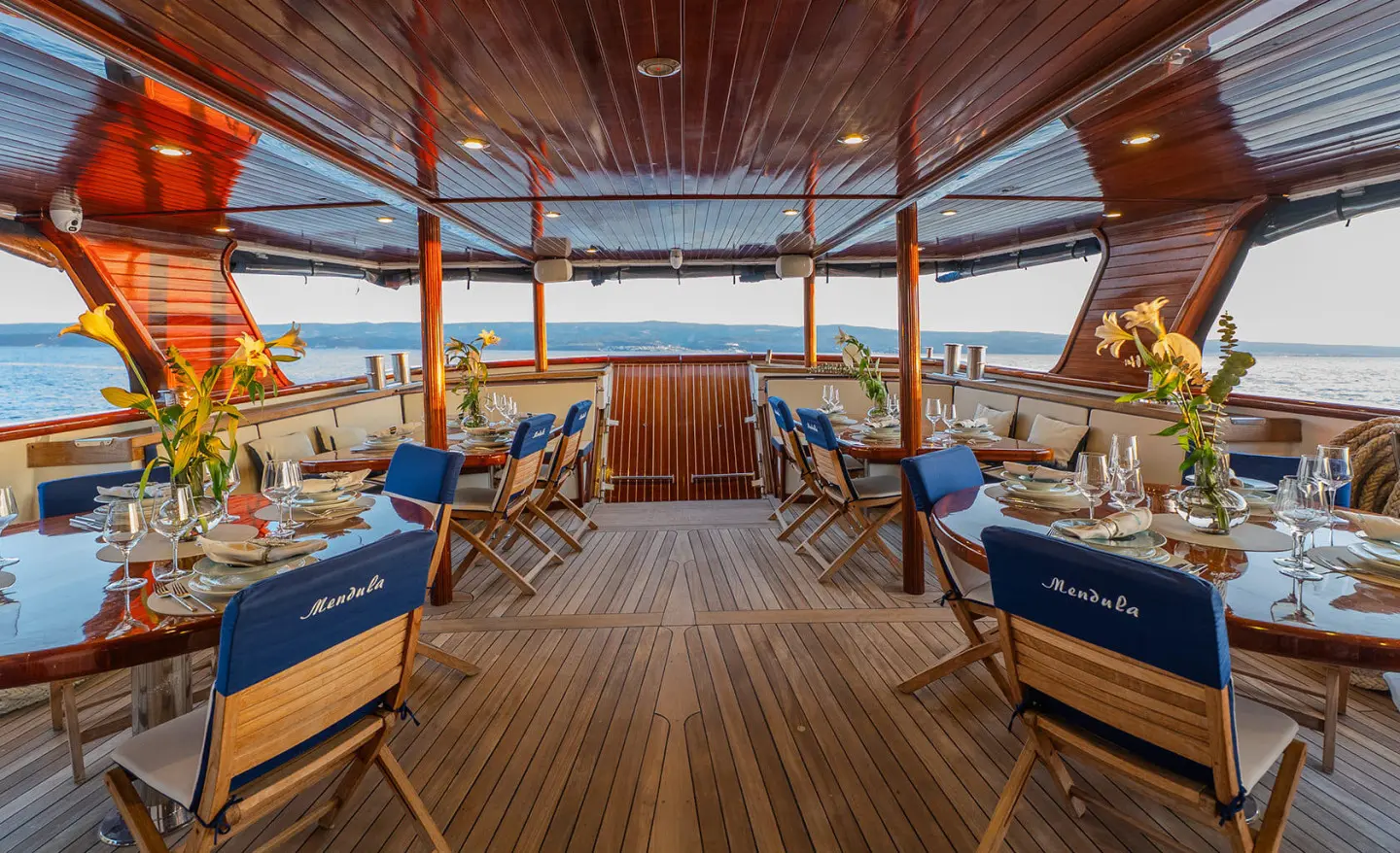 Mendula yacht deck at sunset with wooden floor, blue cushions, and seating