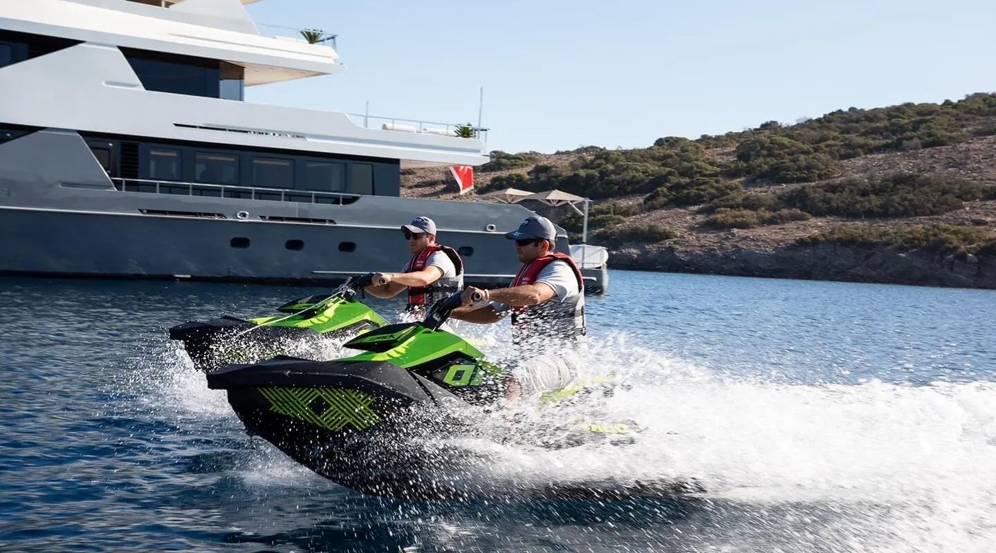 Illusion II yacht anchored with two riders on a green jet ski in clear blue water