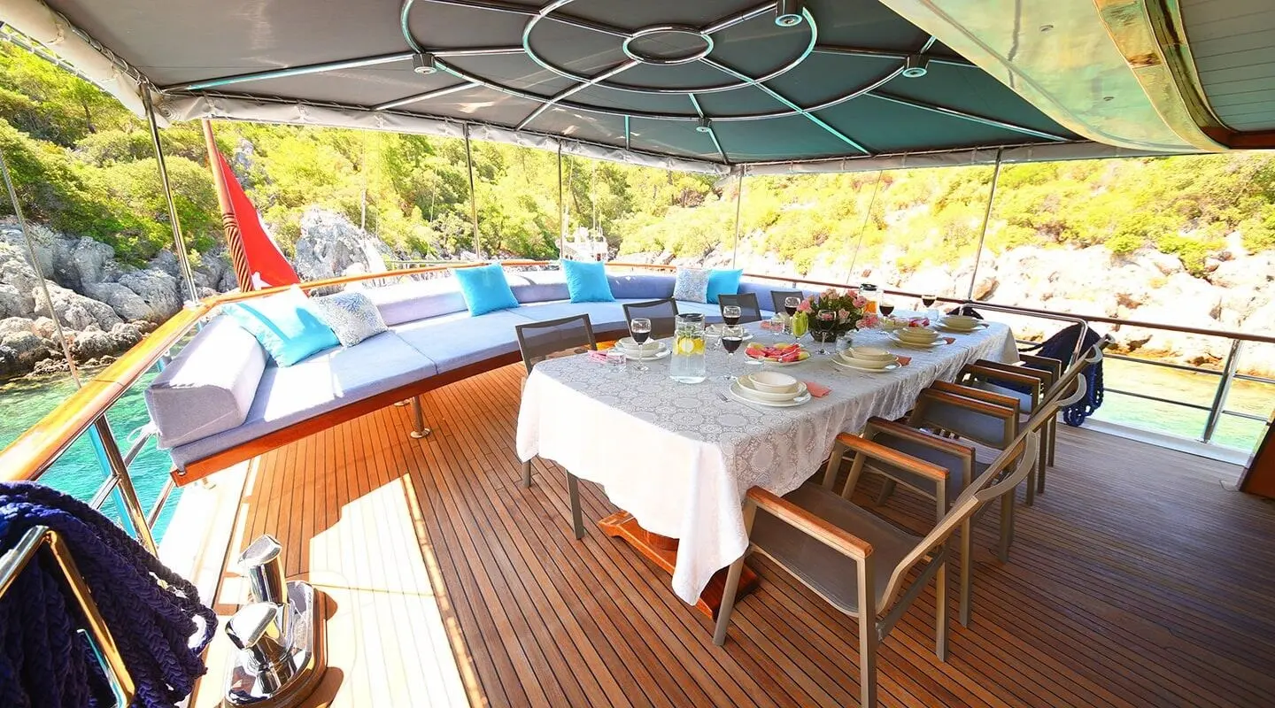 Gulet Maya aft deck with dining table set, sea and rocky shoreline view