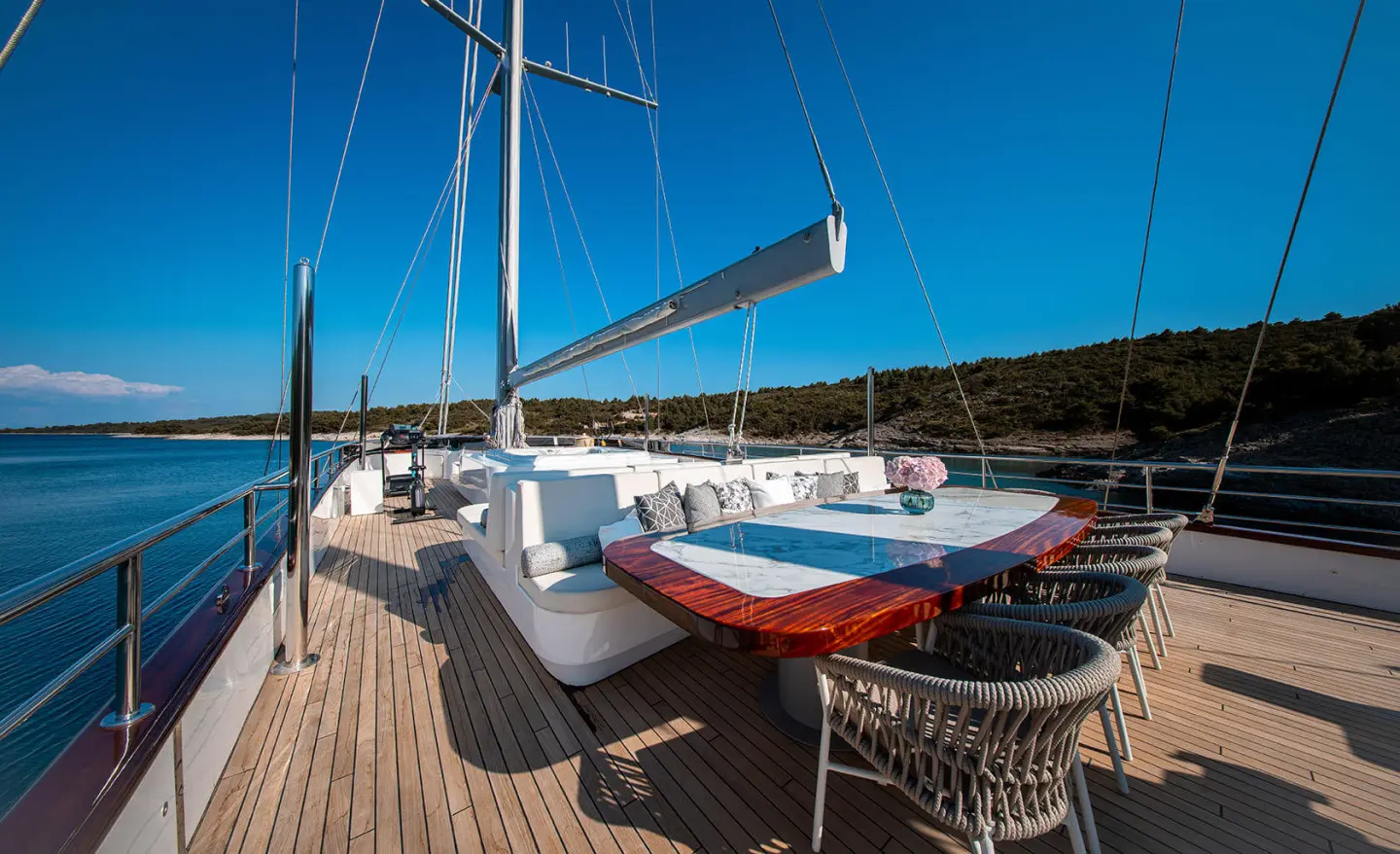 Nocturno yacht deck dining area with wooden deck, table setting, and chairs under blue sky