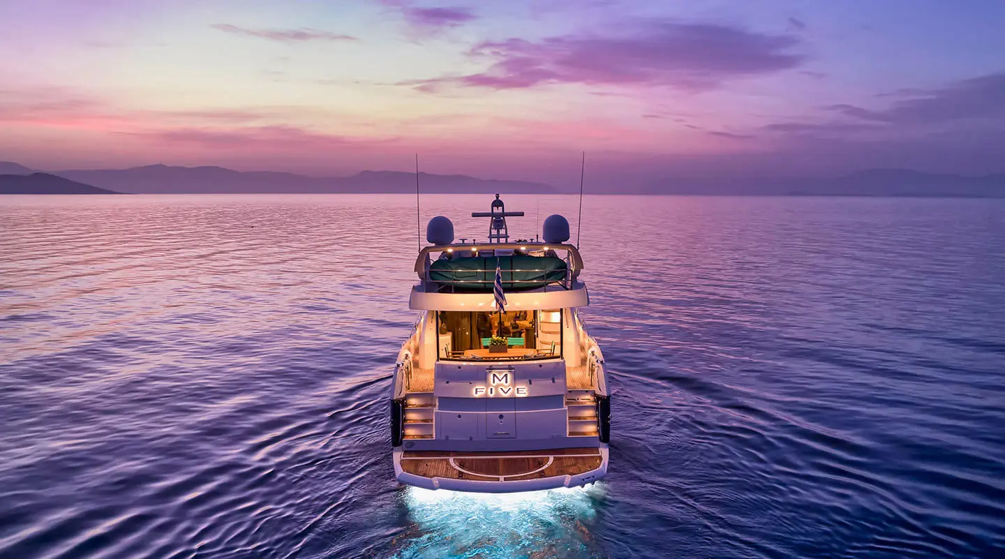 A luxury yacht named M Five sails on calm sunset ocean waters at dusk