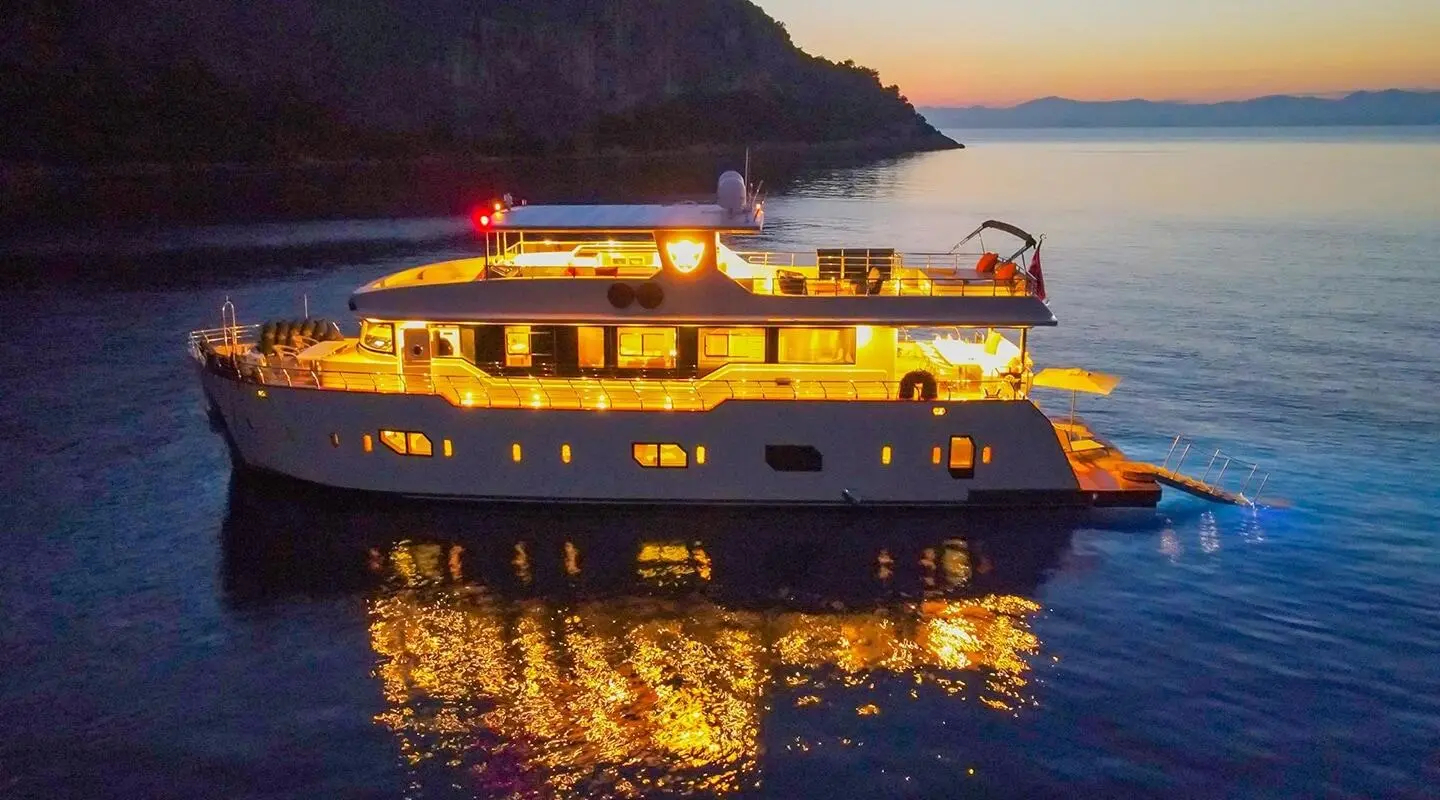 Simay M luxury motor yacht at sunset with calm sea and illuminated deck