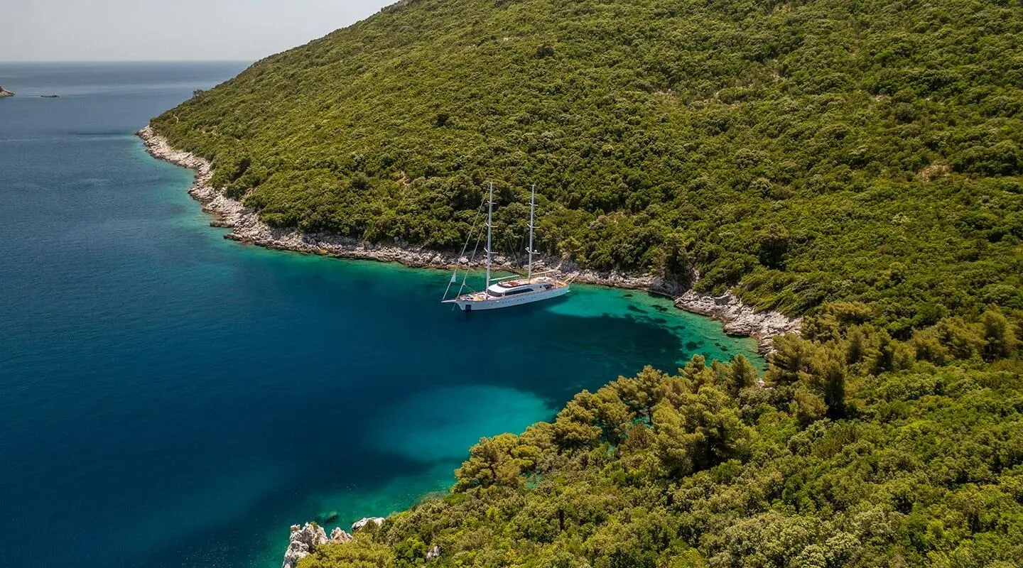 Love Story sailing yacht anchored in a turquoise cove among lush green cliffs