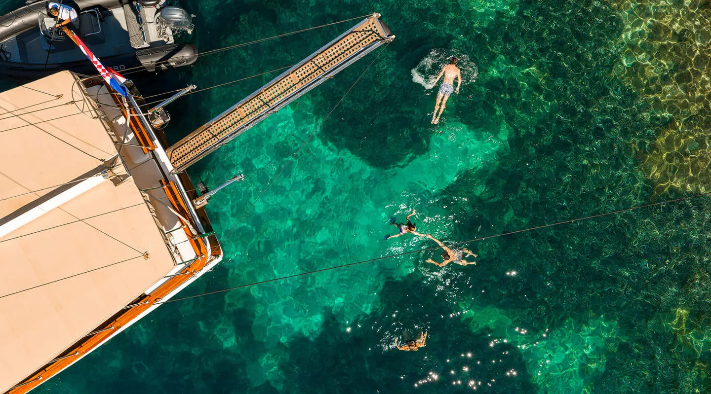 People swimming and deck of Eleganza gulet over turquoise clear water