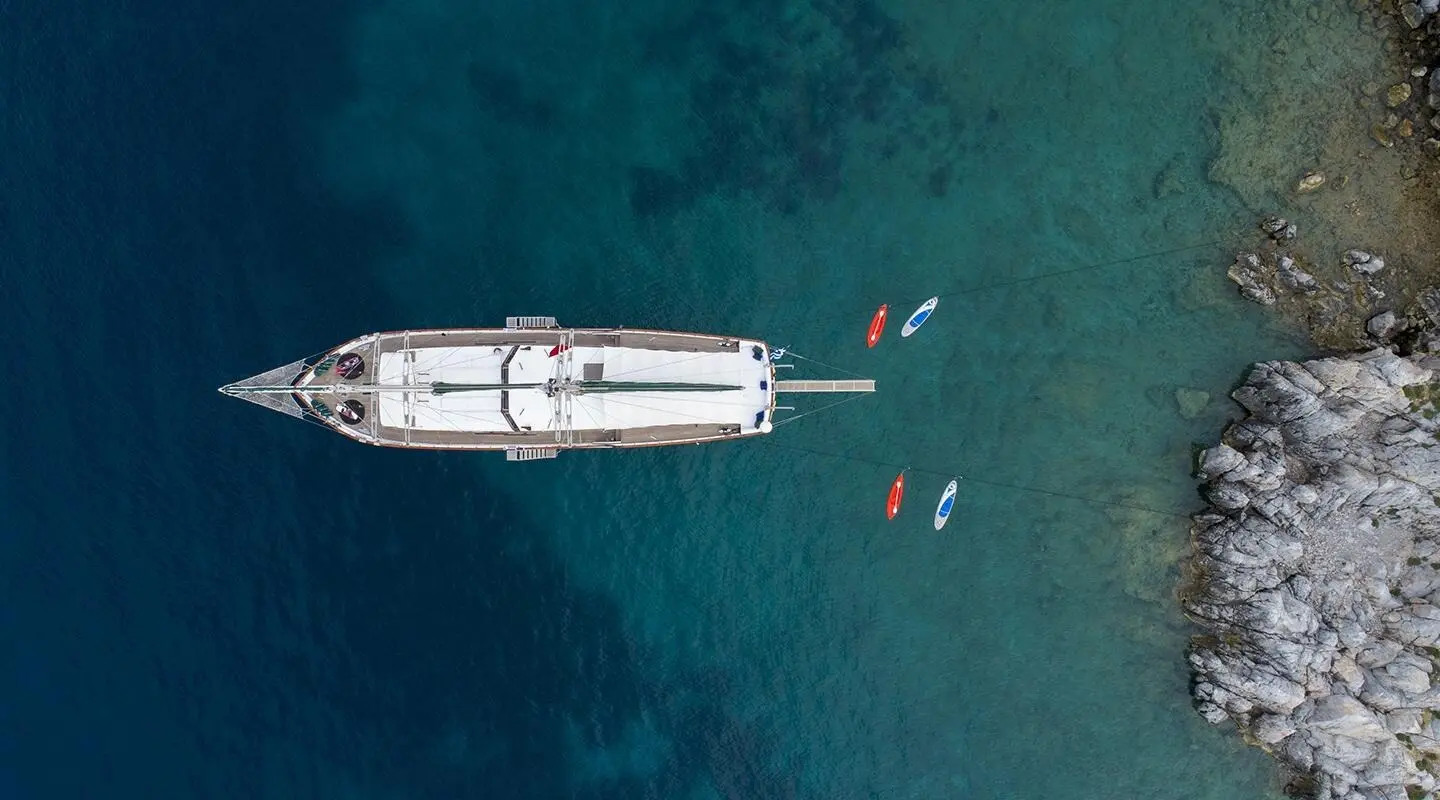 A white luxury motor yacht anchored in clear blue water, viewed from above at sunset