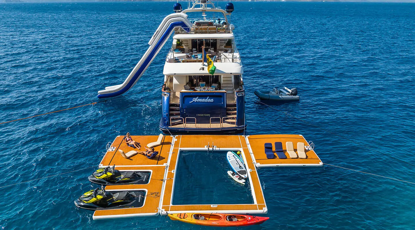 Amadea yacht docked at waterfront with orange tender boats nearby and blue water