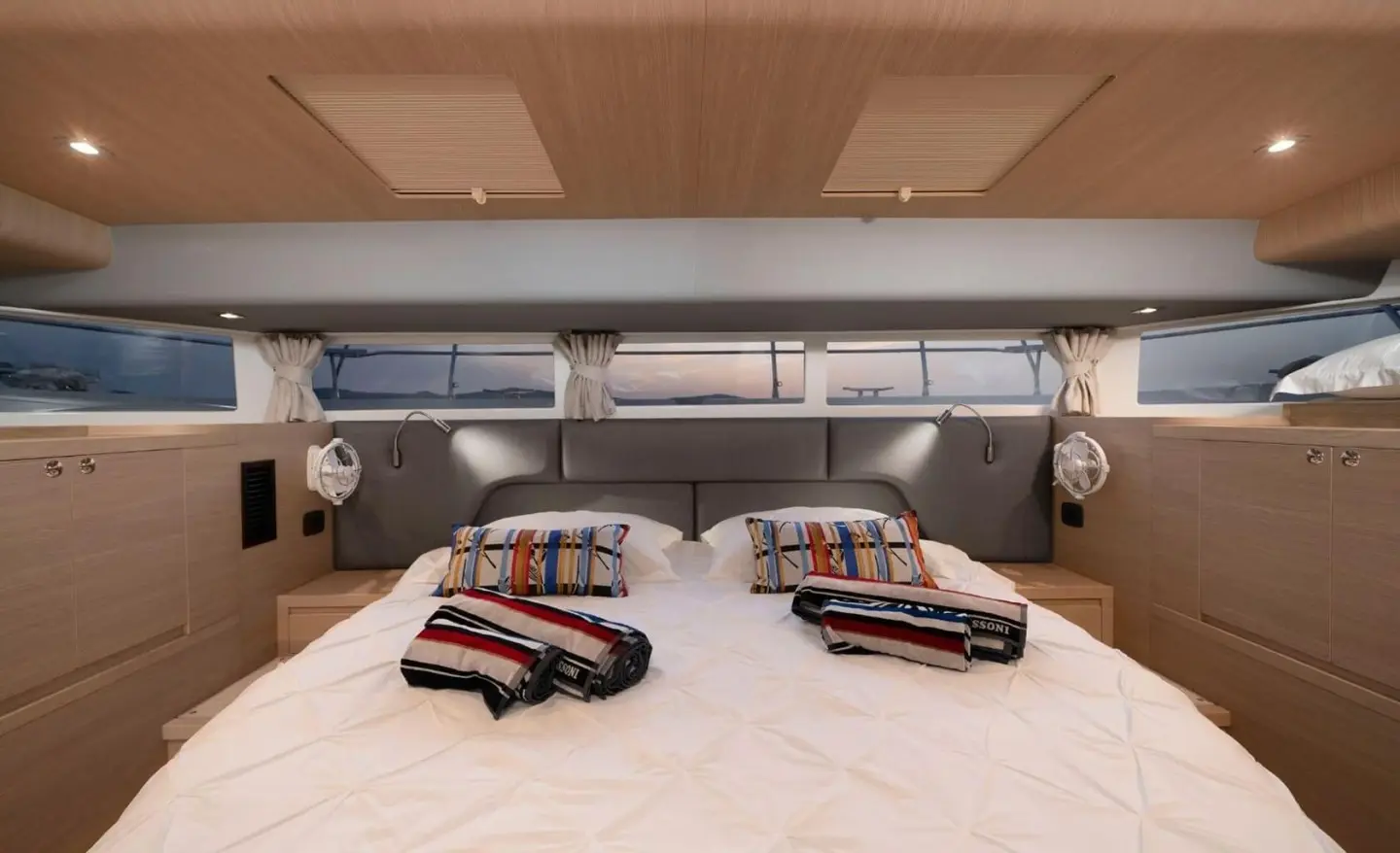 Two beige beds with dark pillows in a luxury yacht cabin under warm lighting