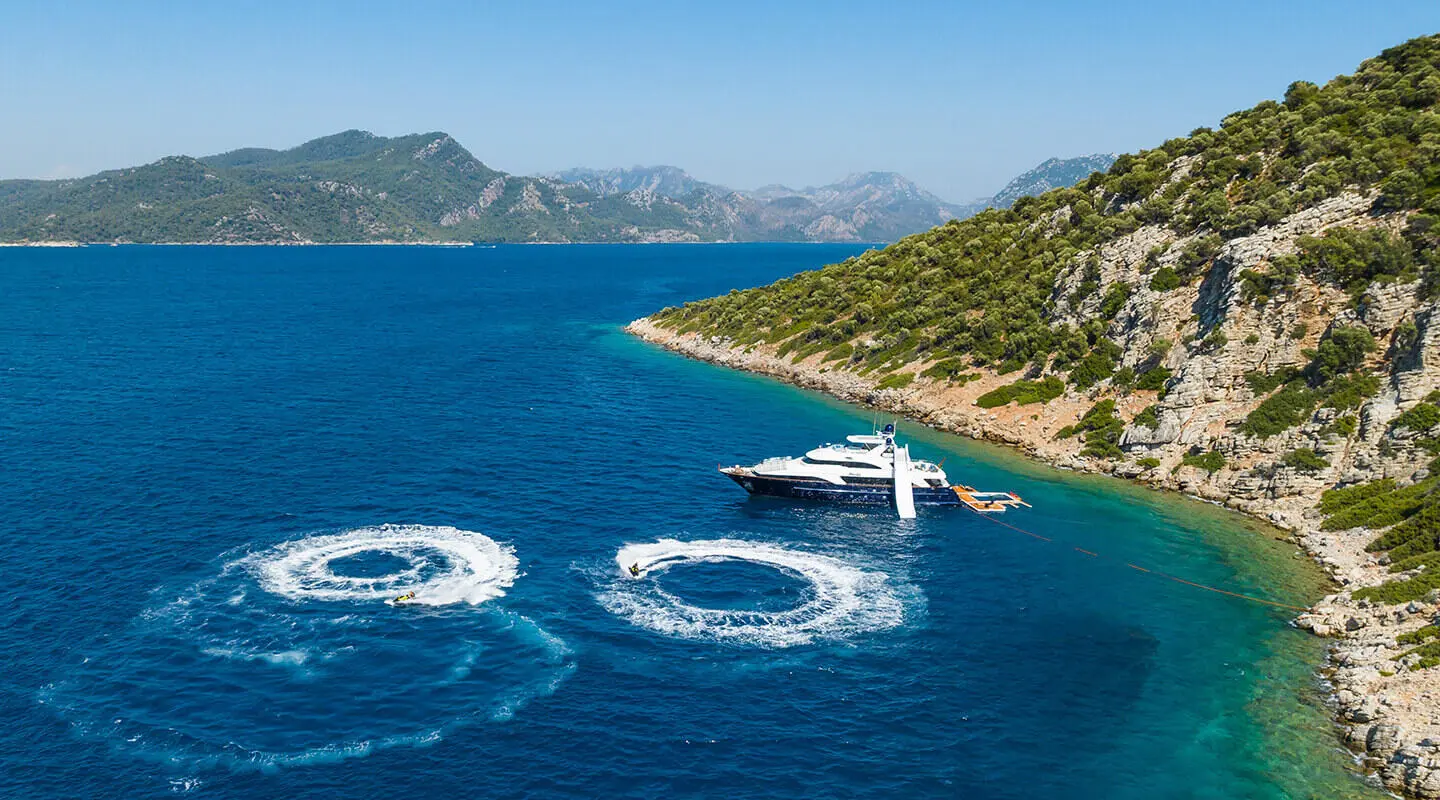 Yacht Amadea docked by a coastal hillside with clear blue water and waves