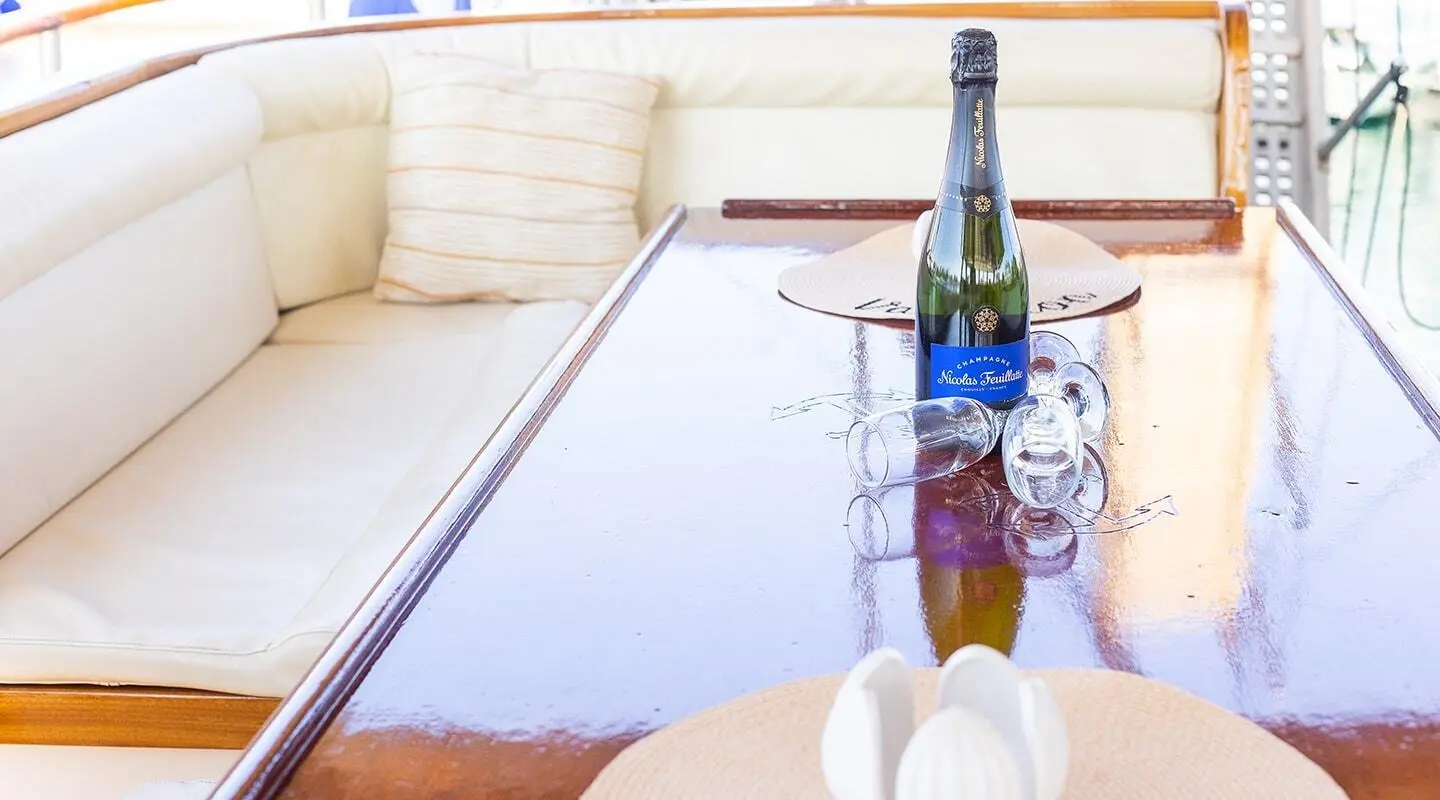Champagne bottle and scattered glasses on a polished wooden table aboard a yacht