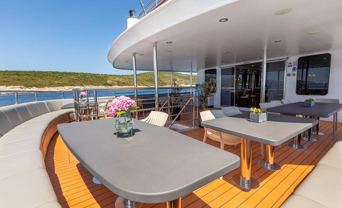 Yacht YOLO on a sunlit deck with a table, white seating, and ocean view