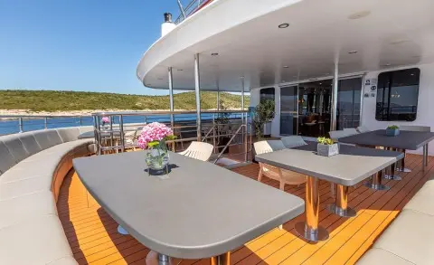 Yacht YOLO on a sunlit deck with a table, white seating, and ocean view