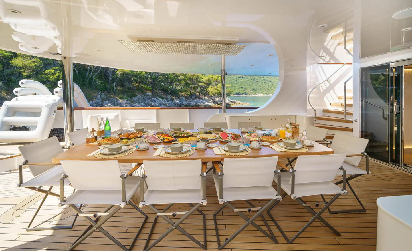 Maia yacht dining on deck with a long table set for guests and views outside