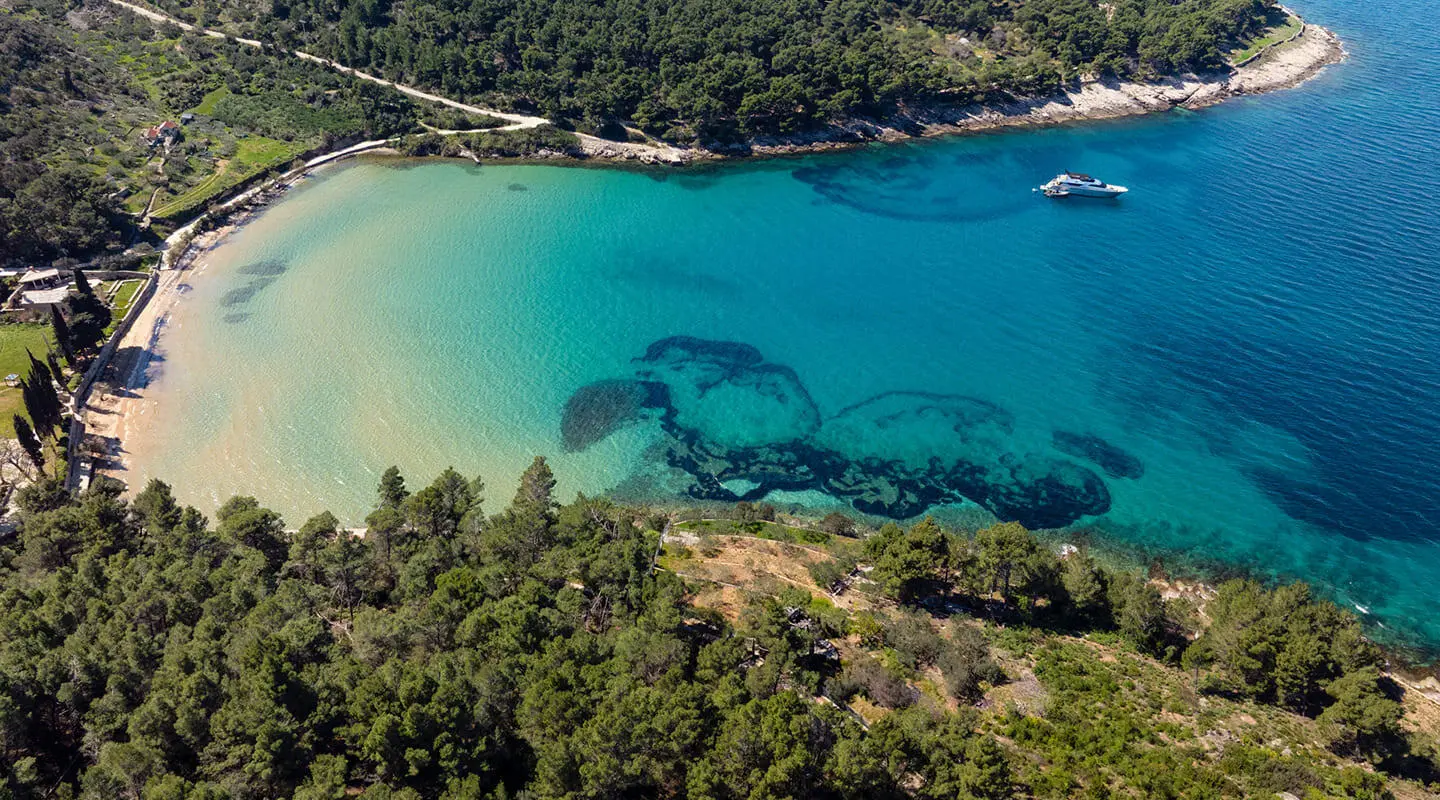 A yacht anchored near a turquoise bay with a forested shoreline