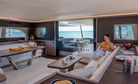 Daiquiri luxury yacht interior: open-plan saloon with white seating, sunlit deck doors, and a woman relaxing on a sofa
