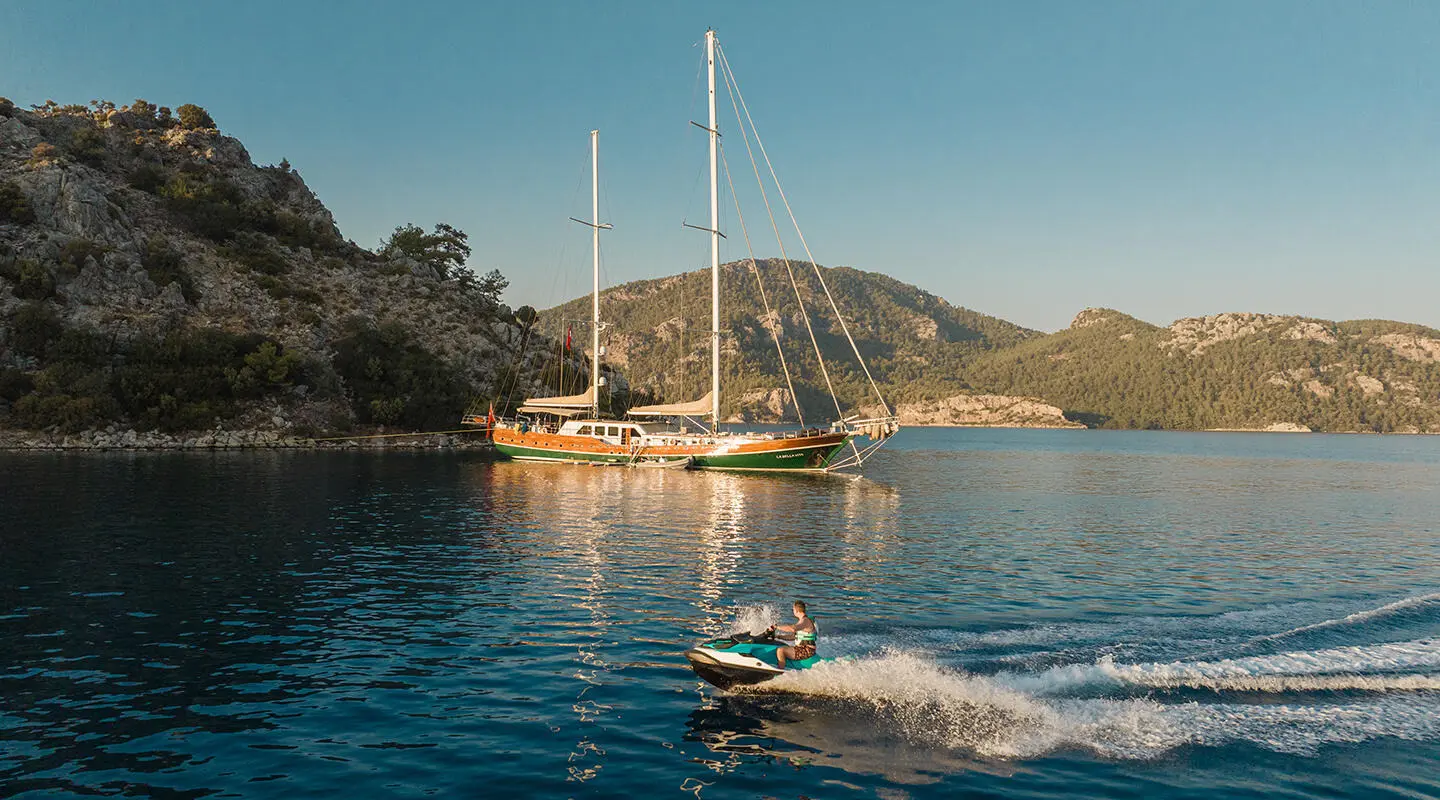 La Bella Vita yacht anchored near rocky coastline at sunset with calm blue water