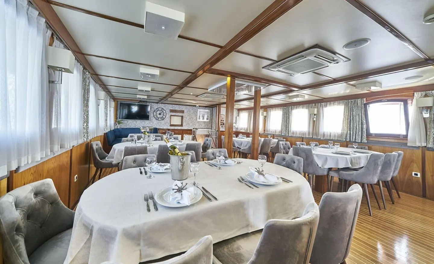 Interior of Amorena yacht dining saloon with round tables, white tablecloths, and wooden beams