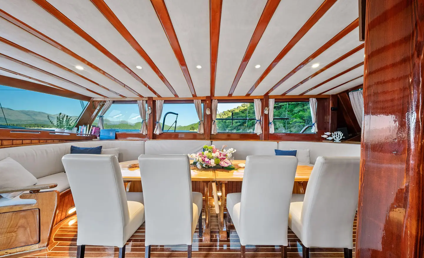 Elegant yacht interior with white chairs around a wooden table under a striped canvas ceiling