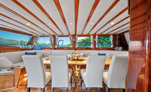 Luxurious interior dining area on Eleganza yacht with a wooden table and cream leather chairs