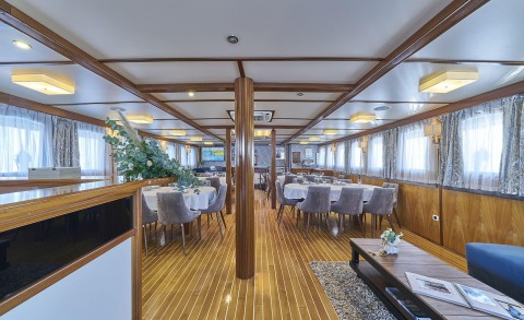 Interior dining area of Amorena yacht with round tables, gray chairs and wood paneling