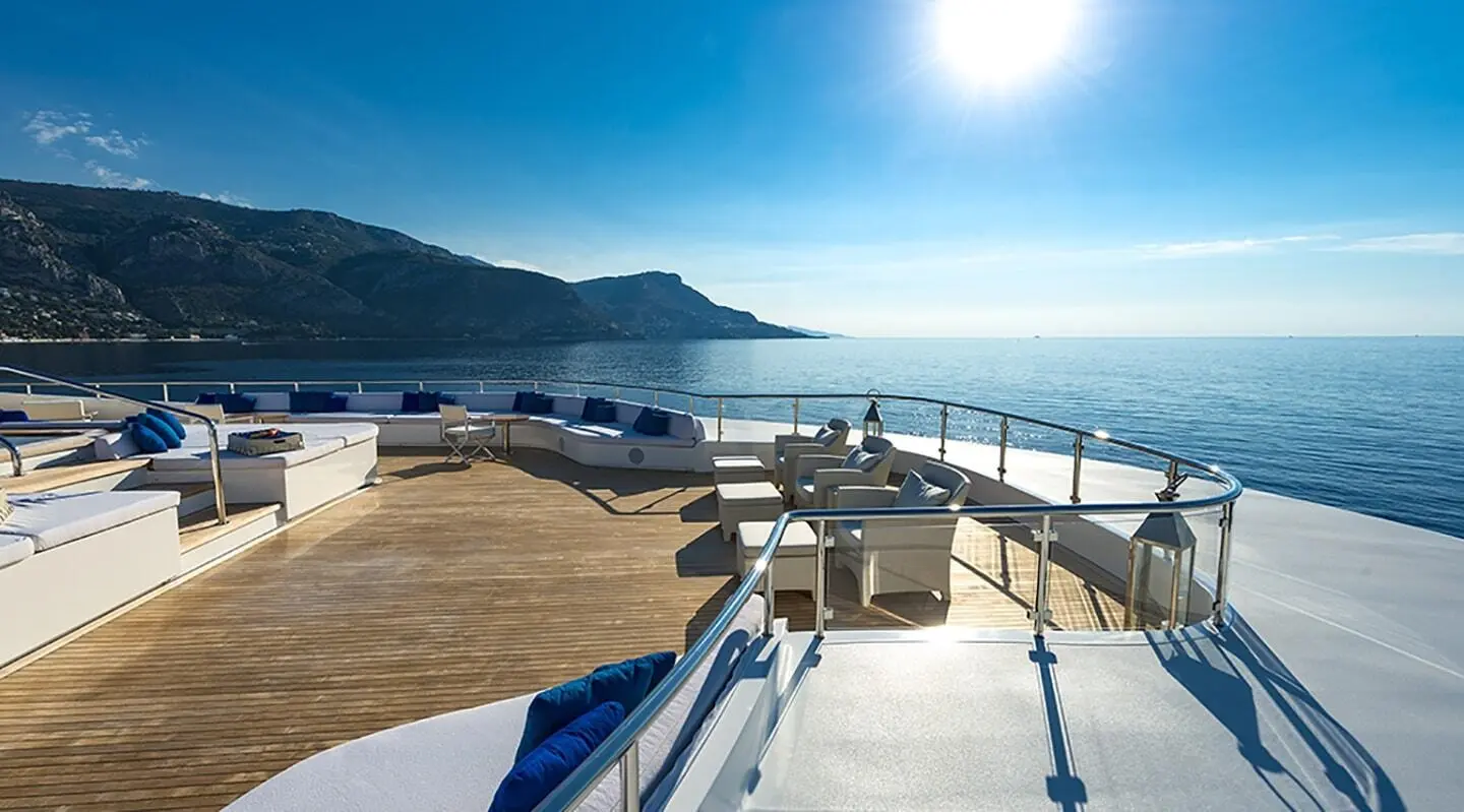 Sunlit yacht deck with seating area and railing overlooking calm blue sea