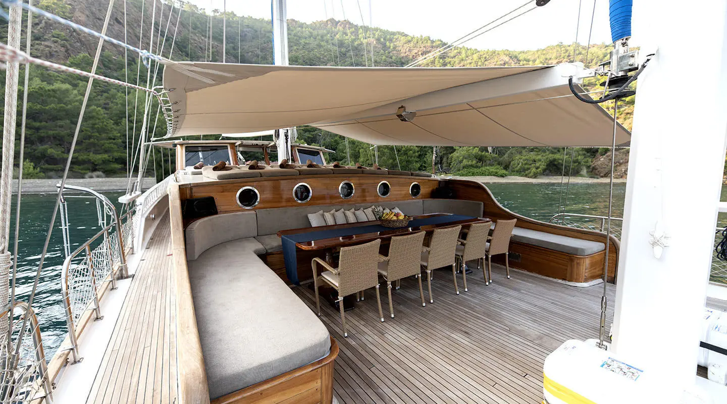 Kayhan 8 yacht charter: wooden deck with table seating under shade sail at sunset