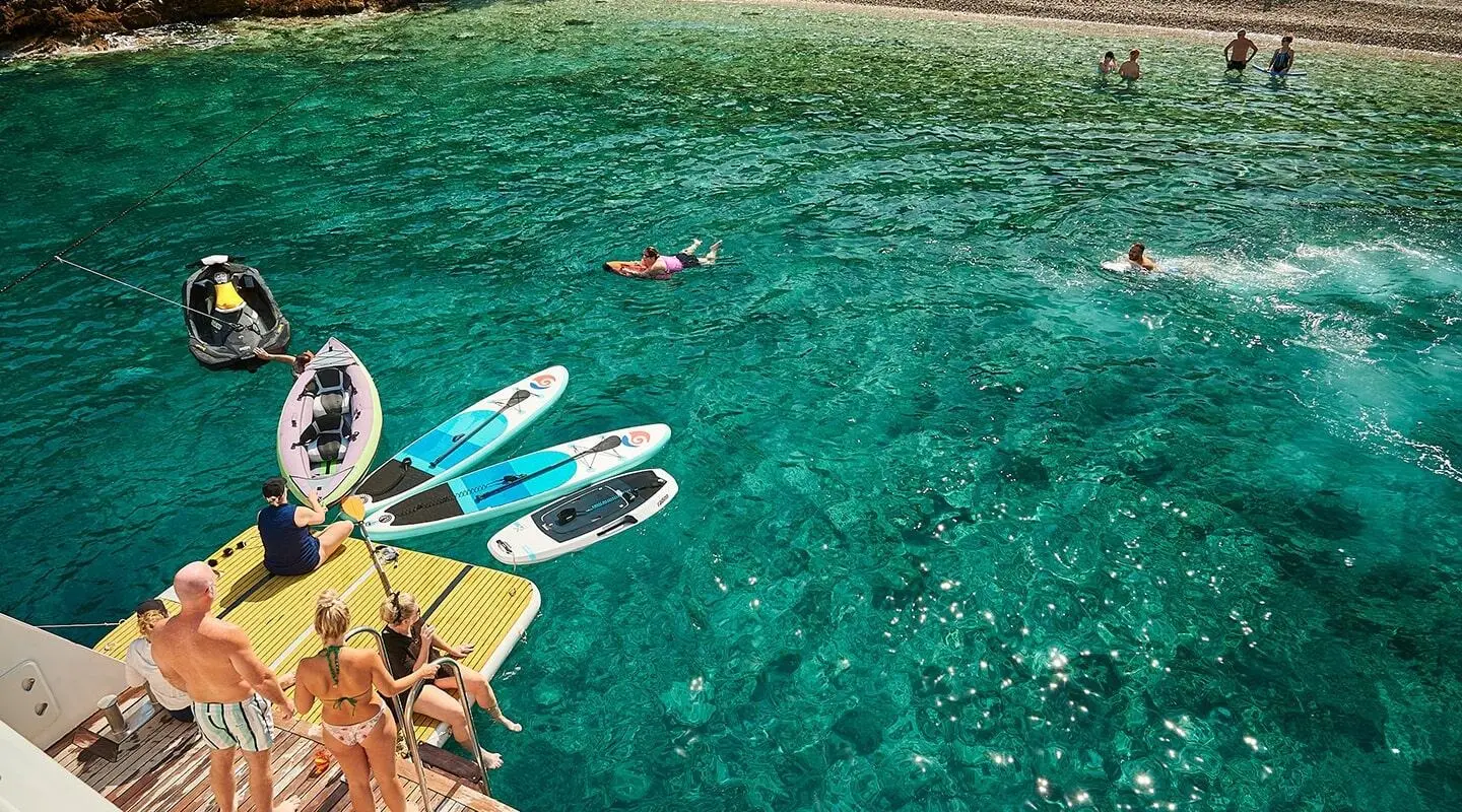 Lupus Mare yacht with kayaks and paddleboards by clear water