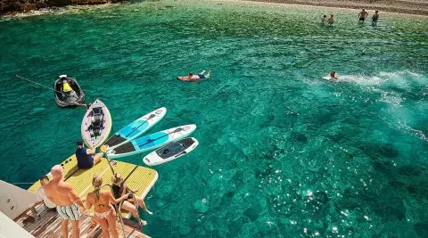 Lupus Mare yacht with kayaks and paddleboards by clear water
