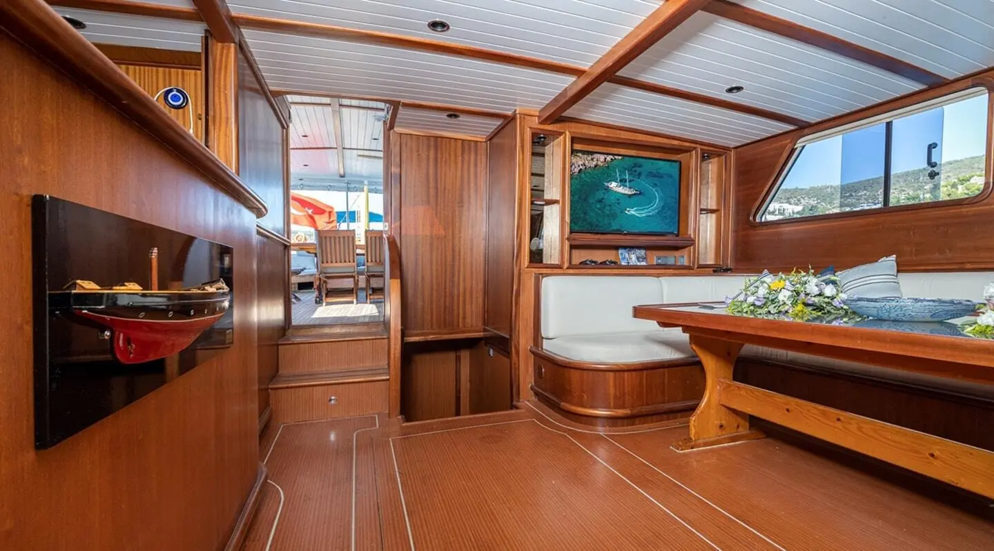 Inside Bodrum Queen yacht with polished wood interior, seating and table, warm lighting