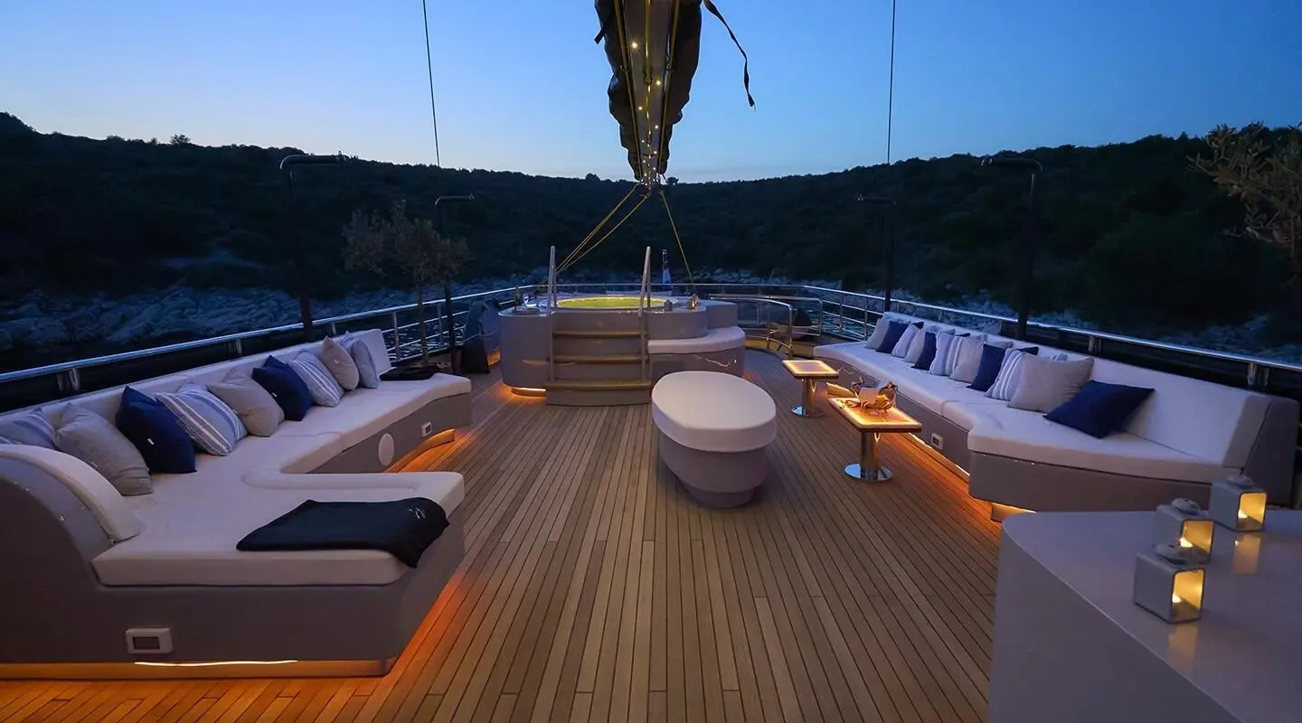 Sunlit yacht deck with seating, teak planks, and blue sea beyond