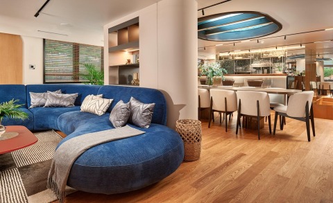 Anetta yacht interior: expansive blue curved sofa, throw pillows, wooden floor, dining area with cream chairs, modern open-plan lounge and bar