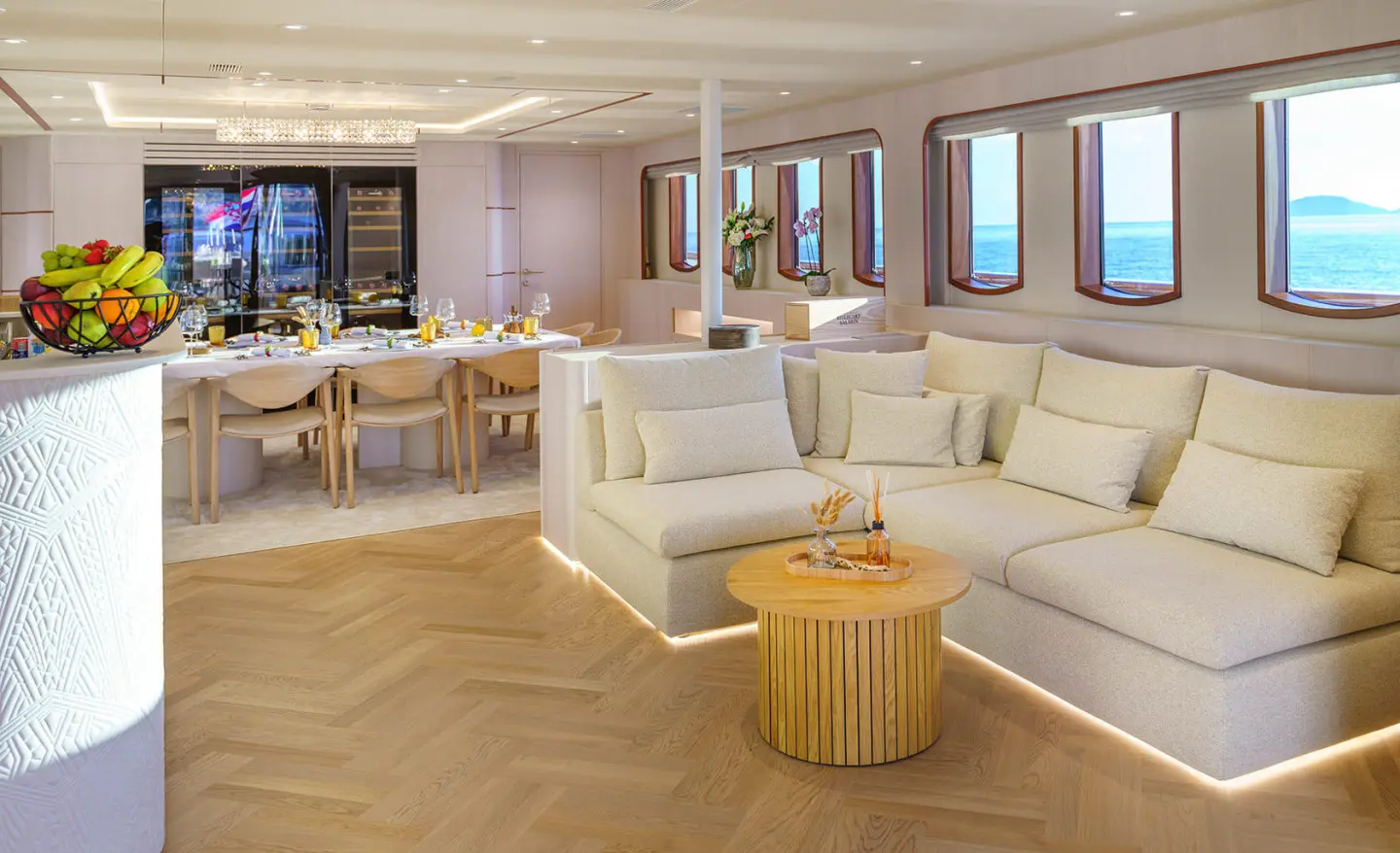 Interior of Maia yacht salon with beige couches, wooden flooring, and windows