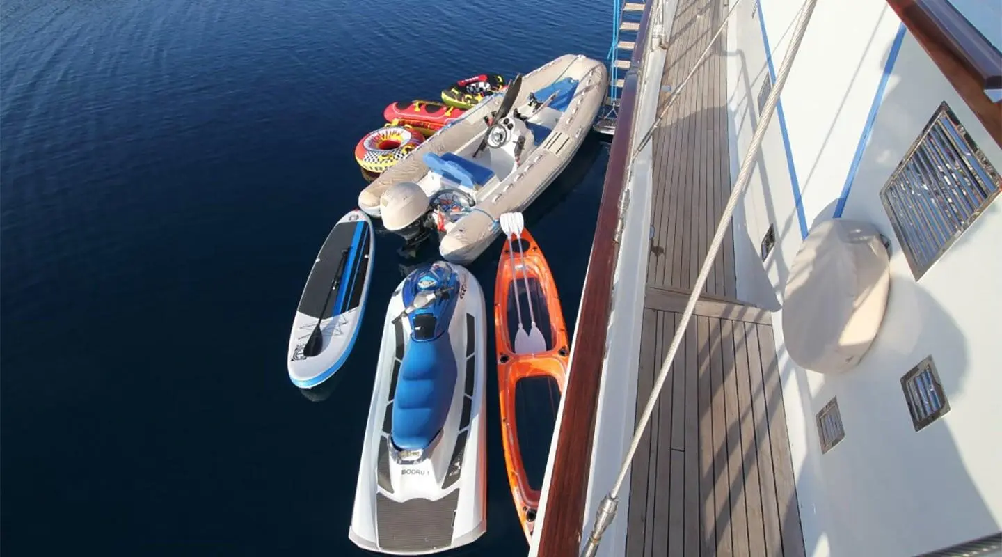 Overhead view of a luxury greenish-blue sailing yacht moored with multiple small boats nearby at dusk