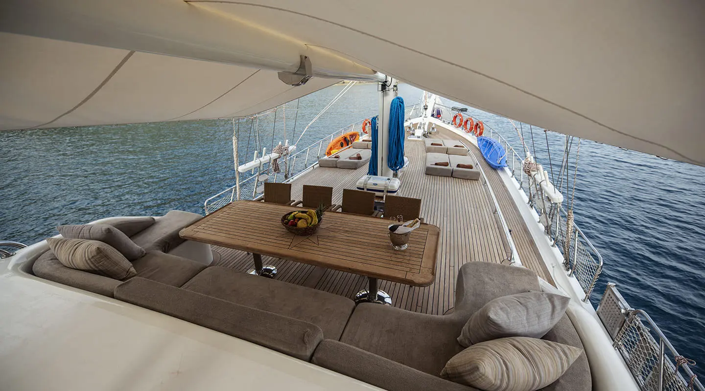 Kayhan 3 gulet lounge area with cushioned seating and a wooden table aboard near calm blue water