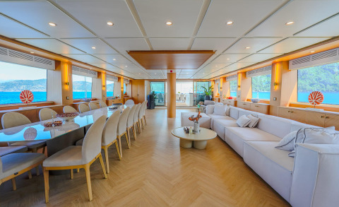King Of The Sea yacht interior with long dining table and white sofas, windows showing sea and coastline