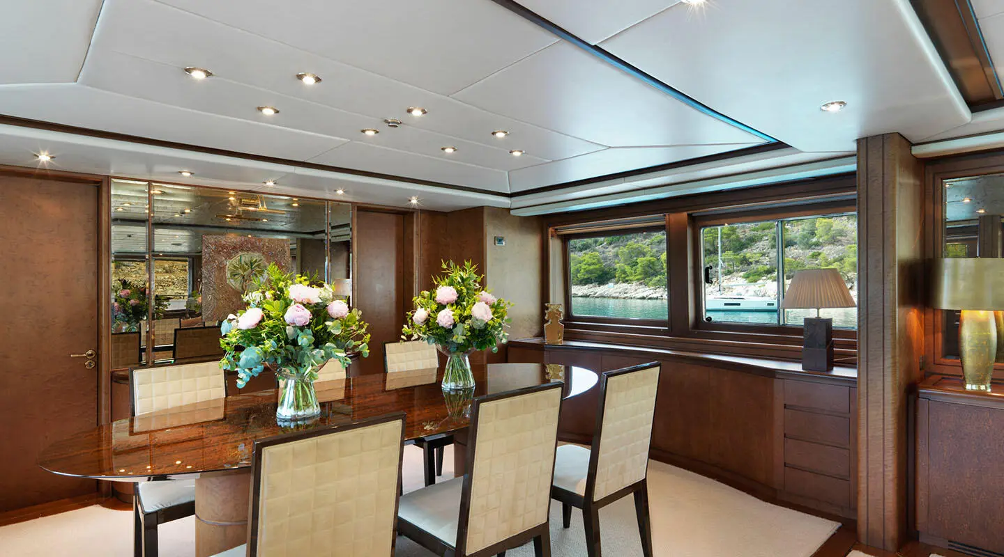 Yacht Idylle dining area aboard: polished wood, long table, white chairs, floral centerpieces and large windows