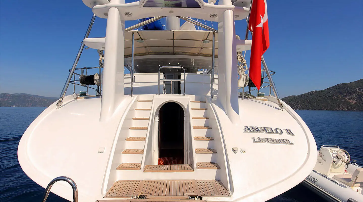 Rear view of Angelo II yacht with stairs, deck ladder, and flag at sunset