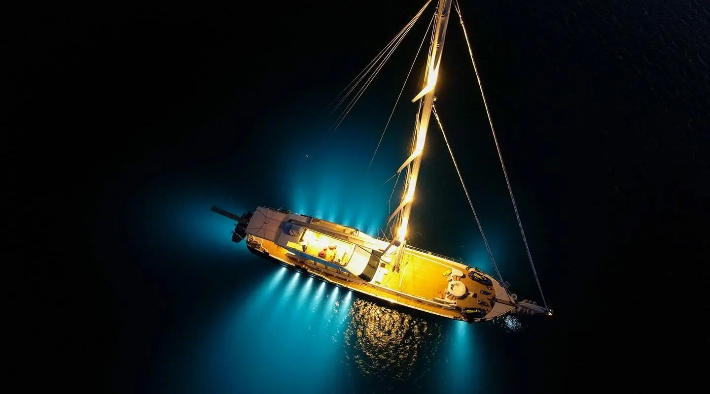 A luxury yacht named Good Life at night, glowing lights in water around hull