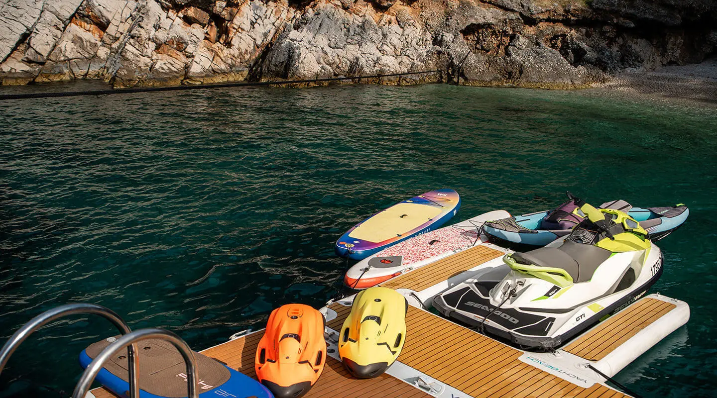 Dalmatino yacht with jet skis and paddleboard on a wooden dock by rocky shore