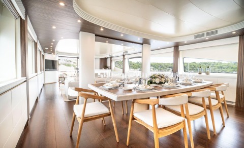 Pareaki II dining saloon aboard yacht with wooden table set for twelve, airy windows, and lush coastal views