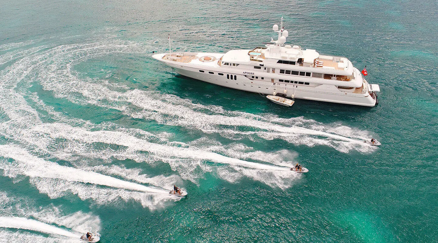 Luxury motor yacht Apogee gliding over turquoise sea with wake and boats nearby
