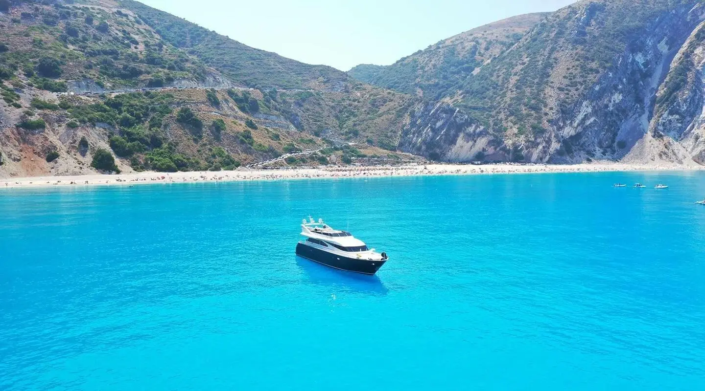 Small luxury yacht named Zoi anchored in turquoise blue bay with cliff backdrop