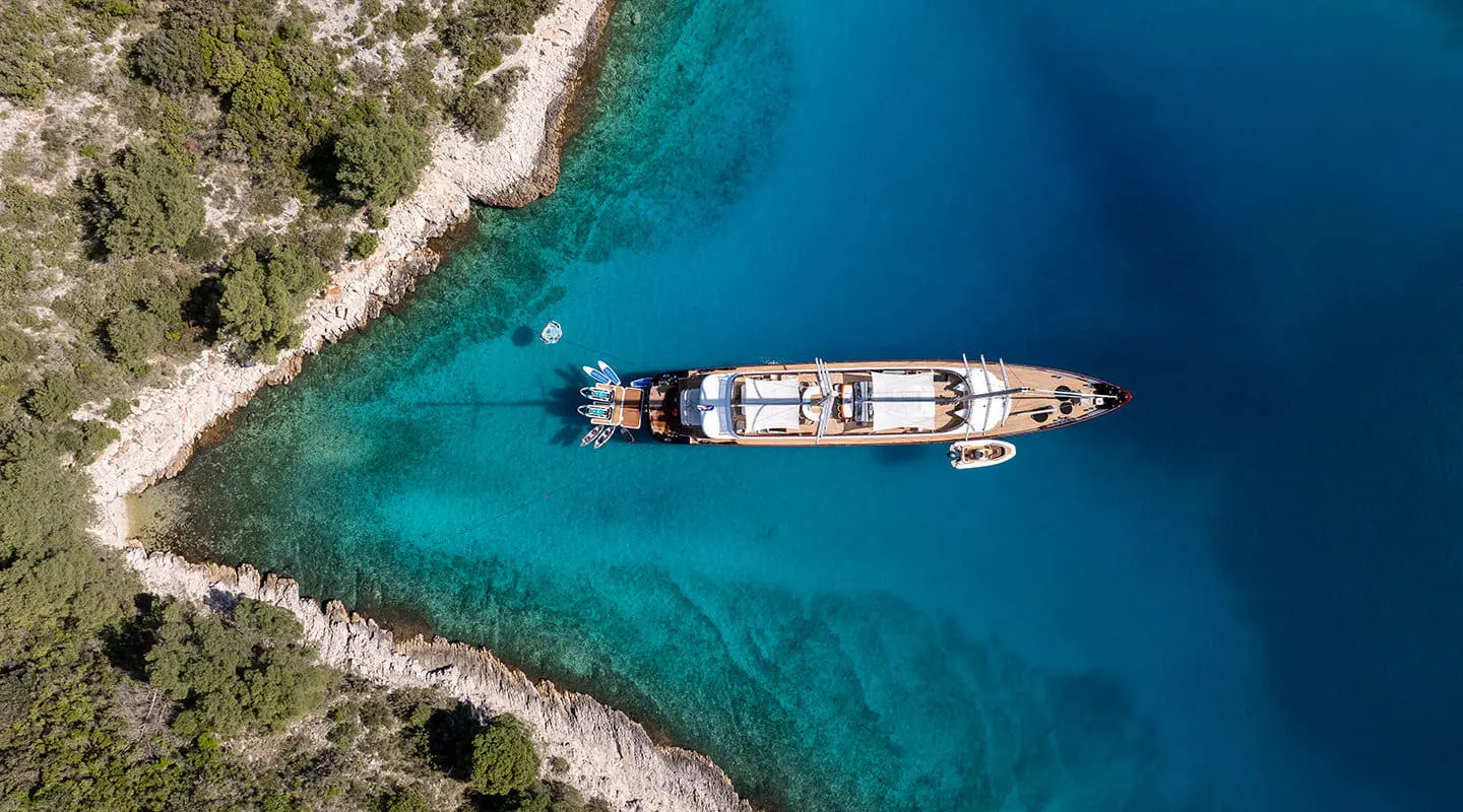 Overhead view of a luxury yacht anchored in clear turquoise water near rocky coast