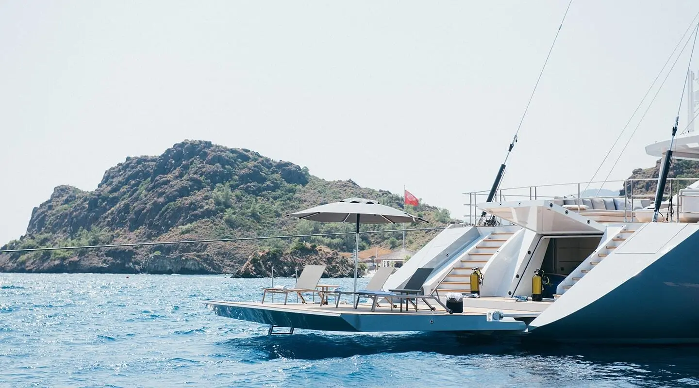 Sunset-lit luxury yacht All About U 2 docked near rocky coastline and hills