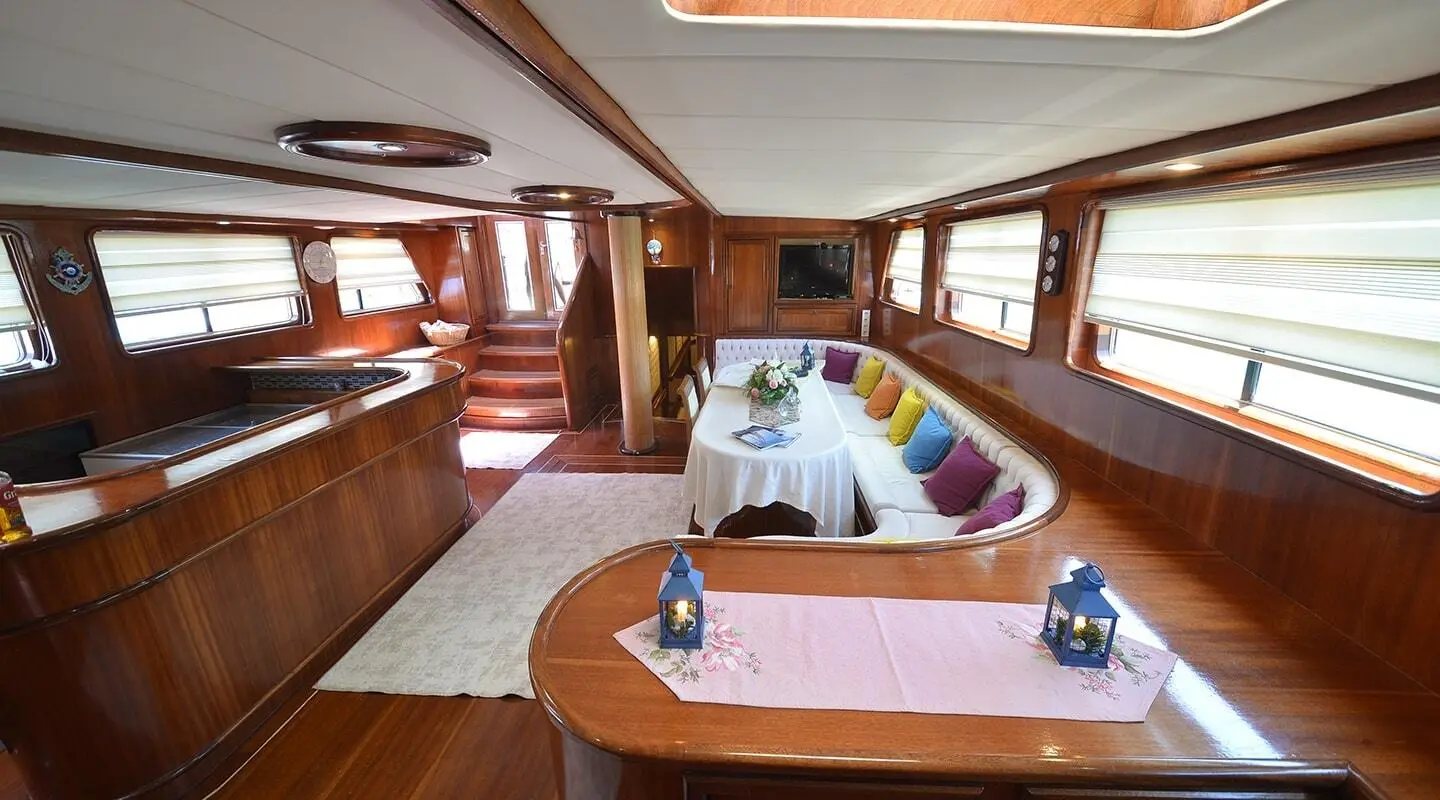 Interior of Prenses Bugce yacht with wooden tables, seating, and a sunlit deck noted.